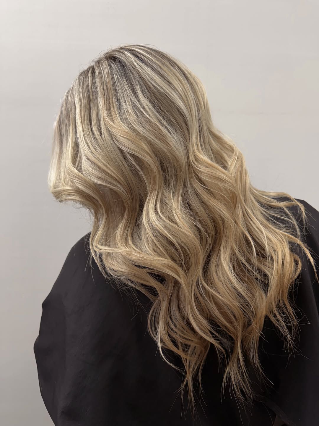Long blonde balayage with a soft natural root, styled in loose waves, photographed from behind