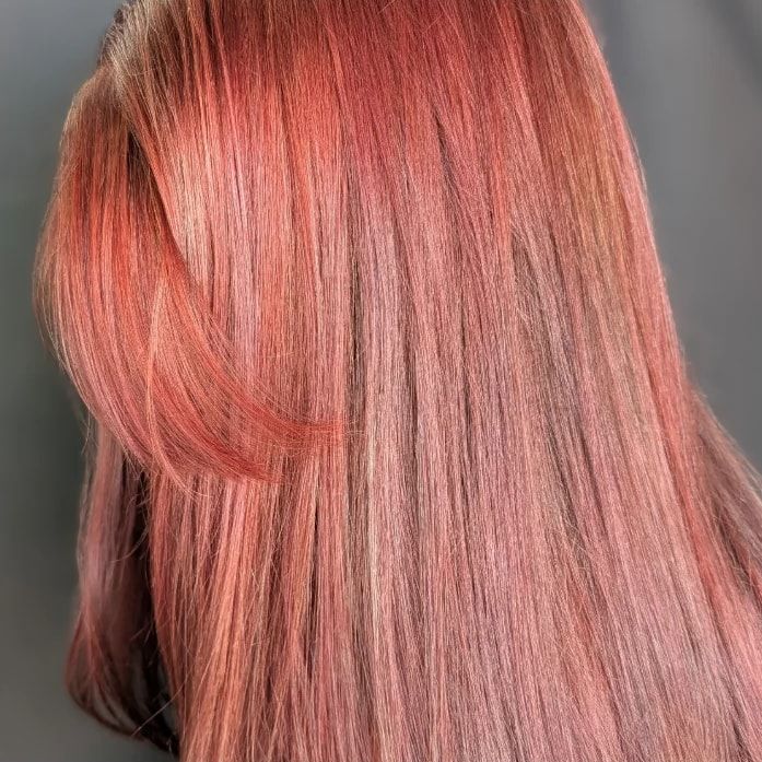 Glossy rose copper hair with soft face-framing layers, seen from the side after a correction from faded teal