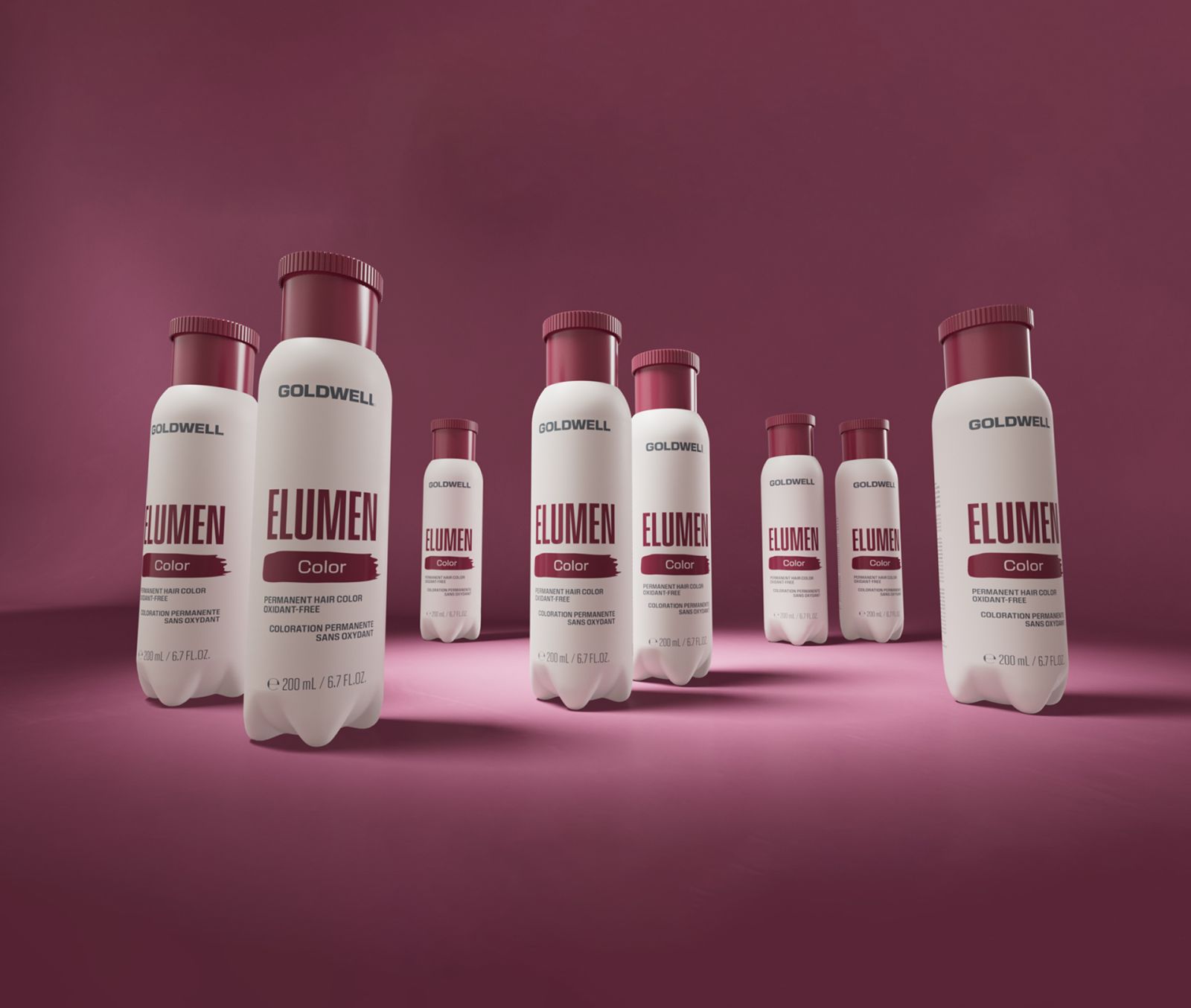 White Goldwell Elumen color bottles with burgundy caps on a magenta studio floor, product photo