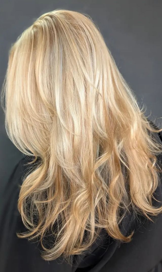 Bright golden blonde hair with soft layers and loose waves, photographed from behind against a dark backdrop