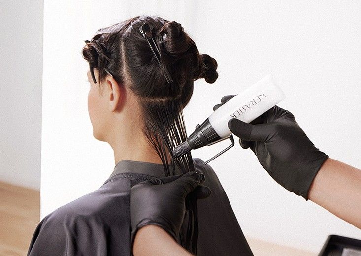 Stylist applying Kerasilk keratin treatment from an applicator bottle to a section of dark hair, Kerasilk brand photo