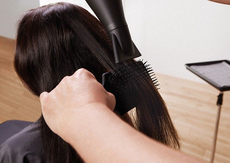 Stylist blow-drying long dark hair with a brush in a salon