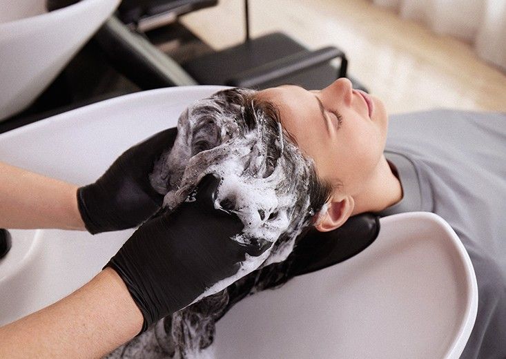 Gloved hands shampooing a client's hair into a foam at the backwash basin, Kerasilk brand photo