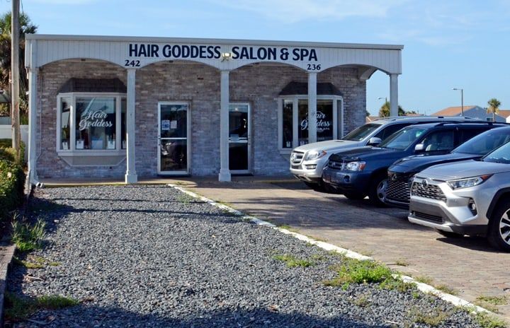 The front of Hair Goddess Salon, Spa & Boutique at 236 Riverbeach Dr., a gray brick storefront with white columns and the Hair Goddess Salon & Spa sign, with parking beside it